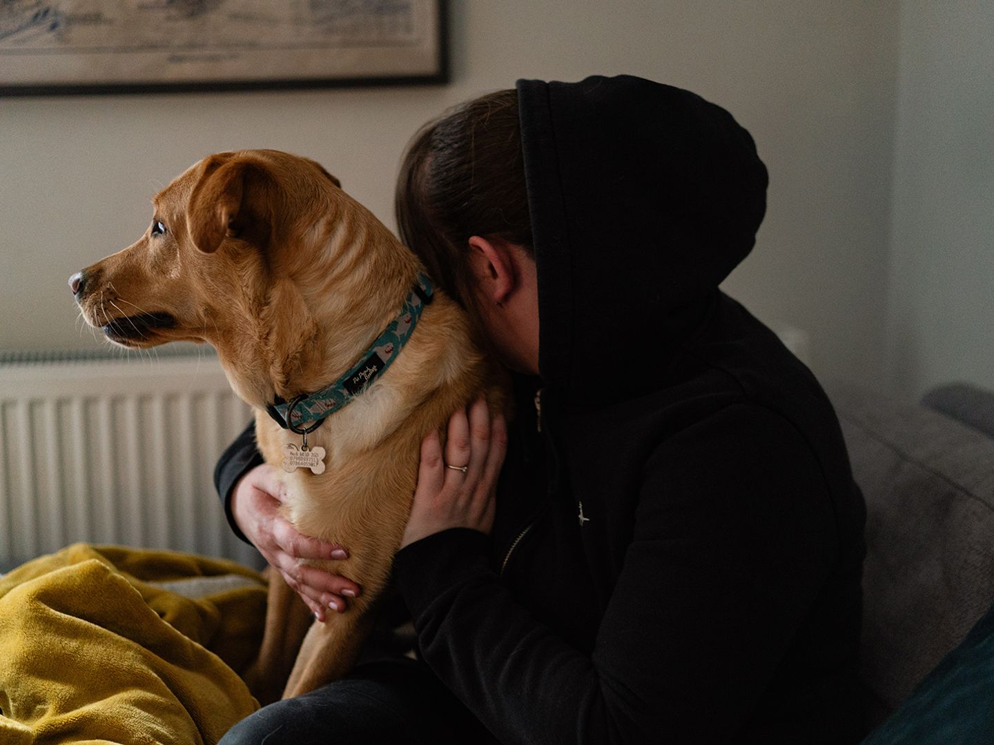 A woman and her golden labrador hug on a bed