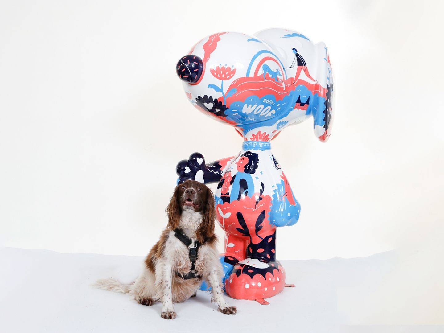 Boris the white and brown Springer Spaniel sitting next to a white, red and blue graffiti designed massive Snoopy statue.