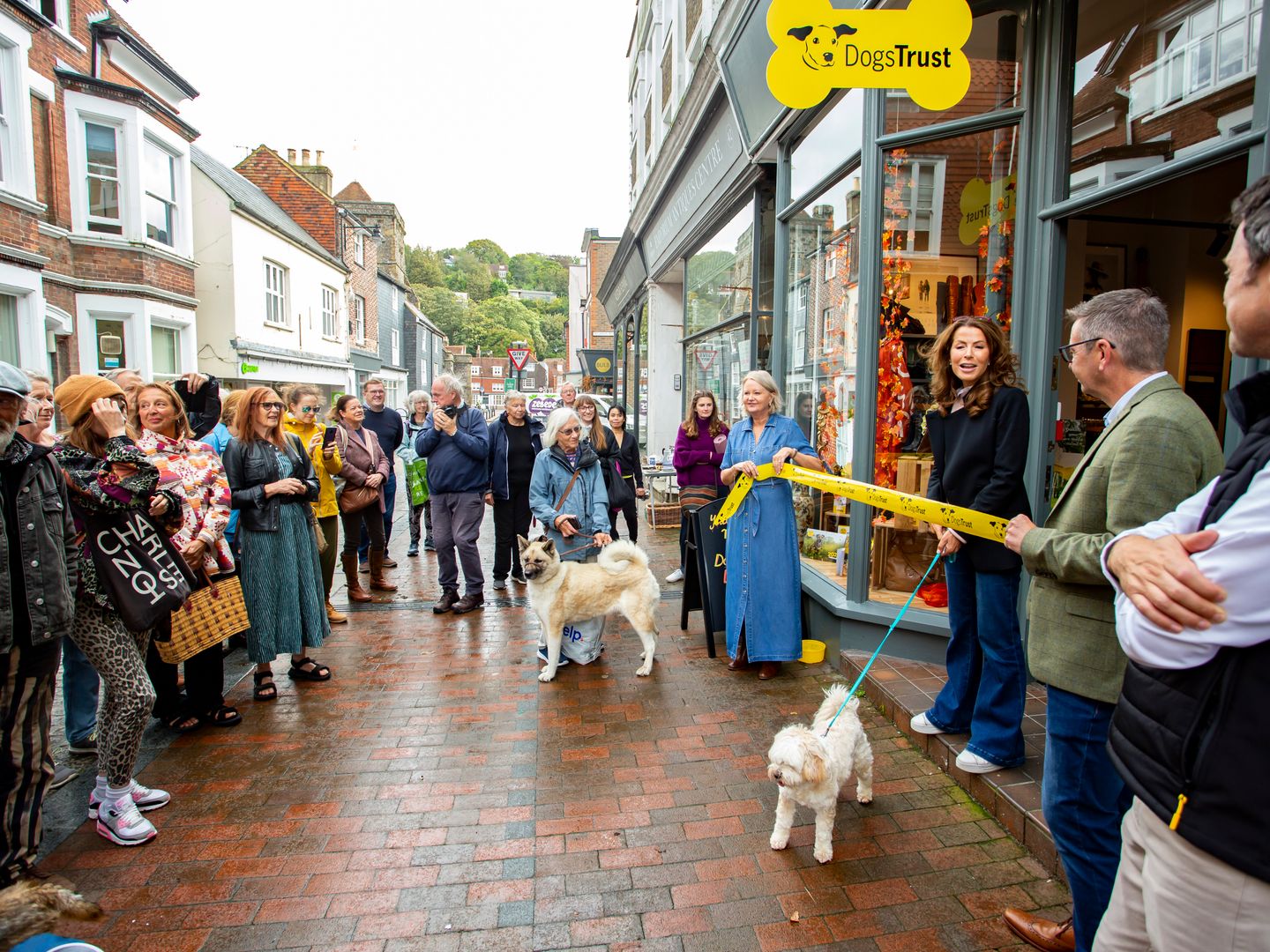 Natasha Kaplinksy cuts a yellow ribbon to open our boutique charity shop in Lewes. She stands in front of a crowd outside smiling with people clapping.