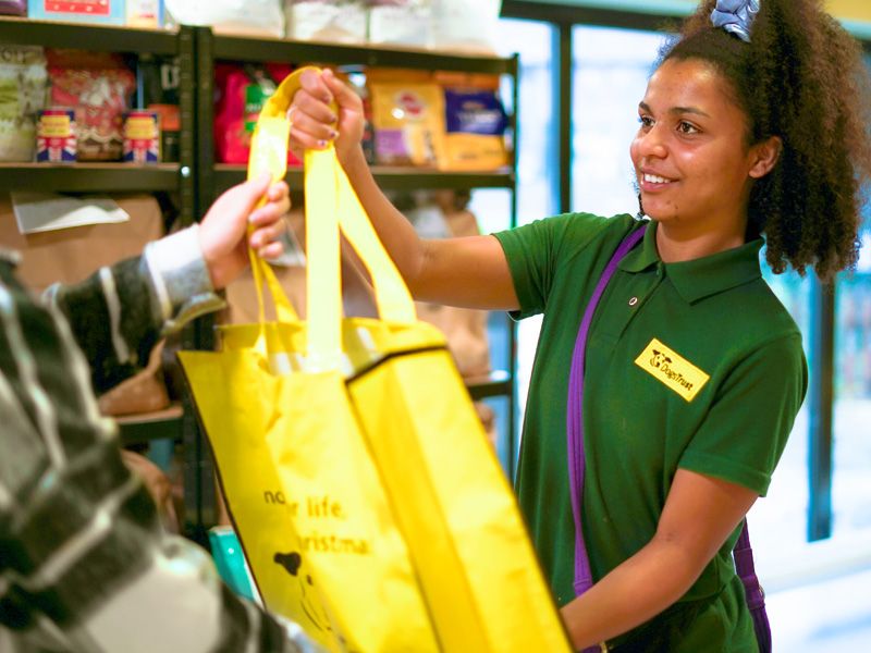 A young lady volunteer wearing a green polo DT shirt holding up a yellow bag that she is giving a visitor at Harefield's food bank.