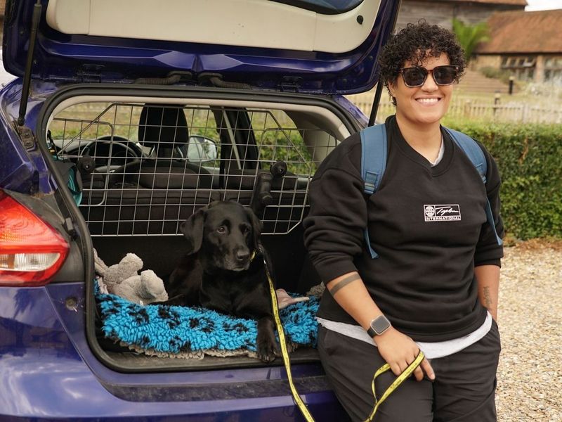 Labrador sat in the boot of a car, new owner smiling to camera holding a dog lead.