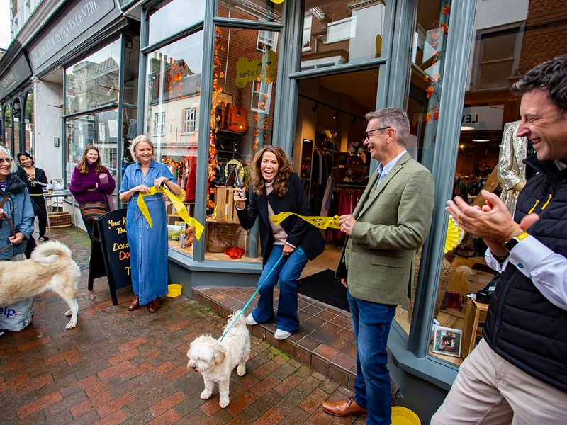 Natasha Kaplinksy cuts a yellow ribbon to open our boutique charity shop in Lewes. She stands in front of a crowd outside smiling with people clapping.