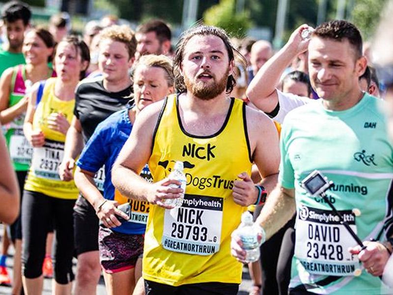 A male runner wearing a yellow running vest and looking at the camera amongst a sea of runners whilst running at Manchester 10k